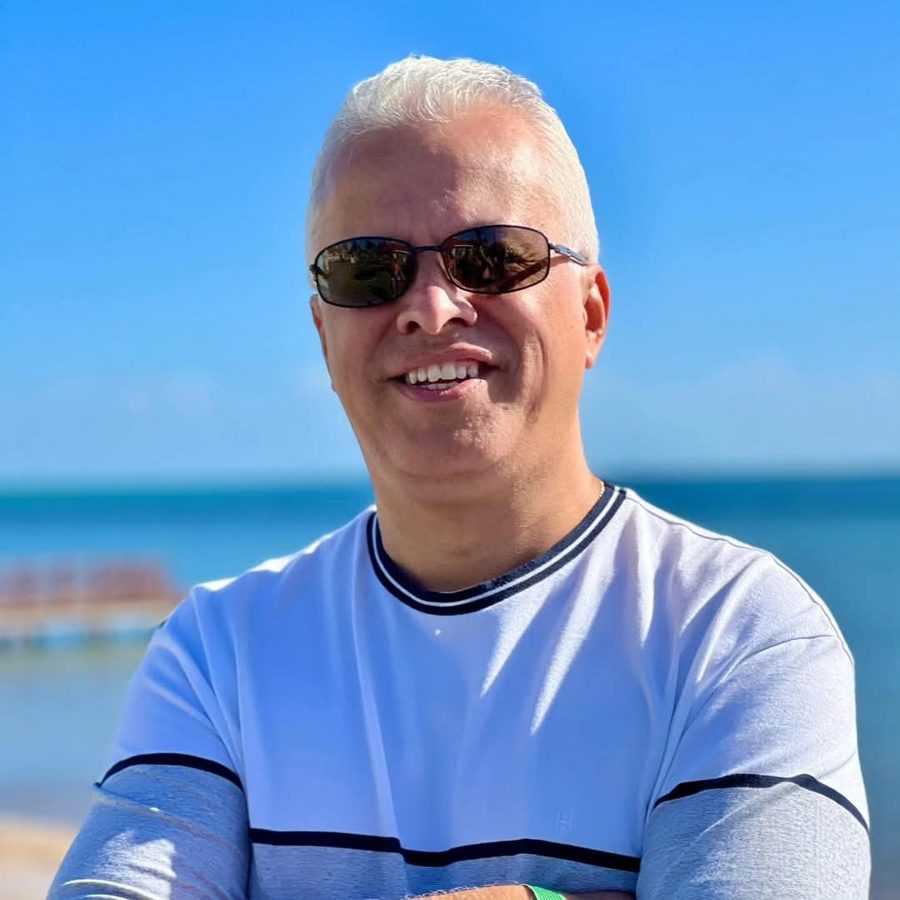 Fábio Pereira sorrindo, de óculos escuros, com o mar ao fundo